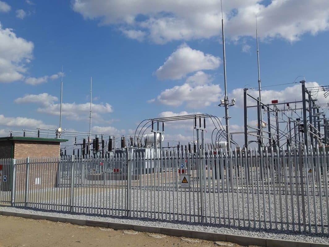 A completed, fenced substation yard with control building under a cloudy sky