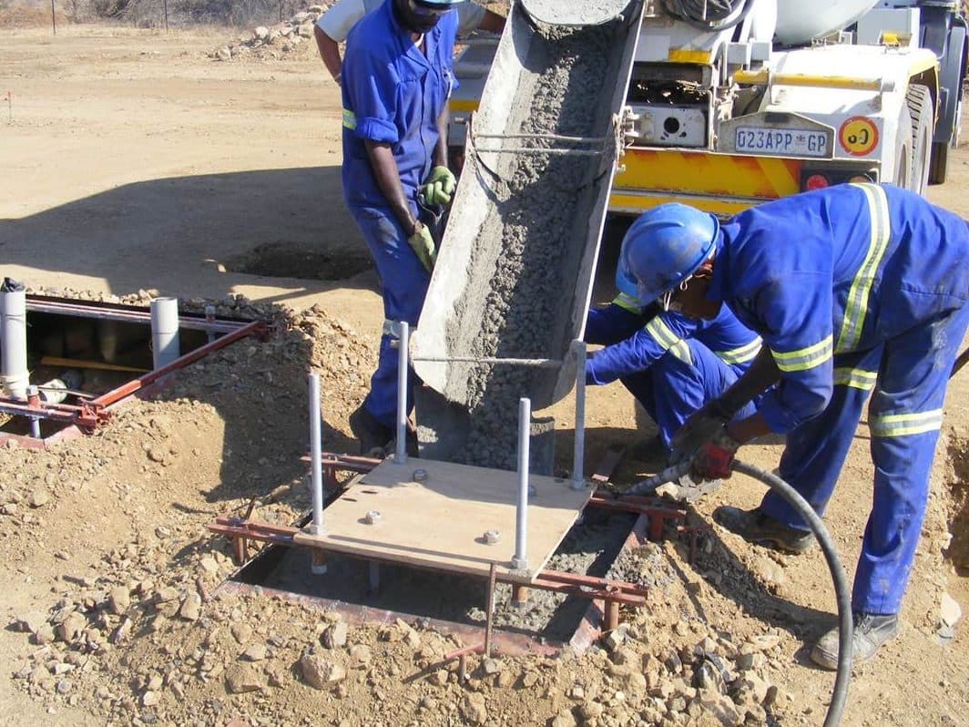 Crew members in overalls and hard hats casting a concrete foundation
